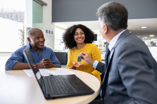 Salesman at the dealership giving the keys of a car to a woman with her father