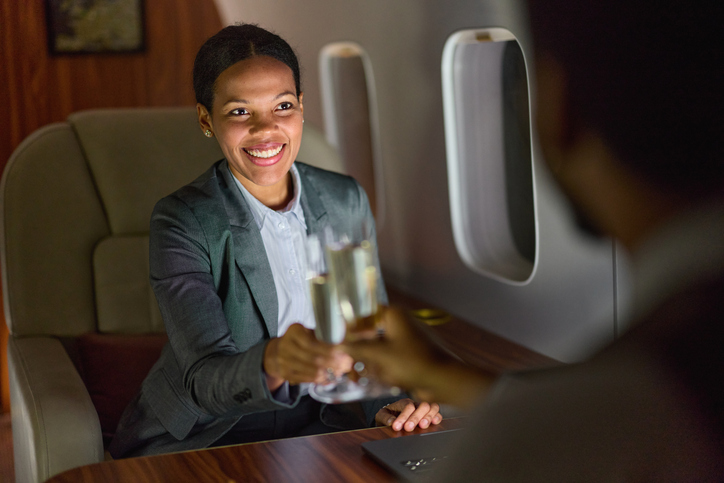 Happy black businesswoman toasting with her colleague during night flight by private jet.
