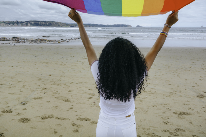 Woman holding the Gay Rainbow Flag on the beach outdoors. Happiness, freedom and love concept for same sex couples. Image