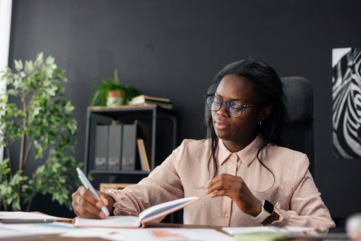 Black businesswoman writing in notebook at office desk