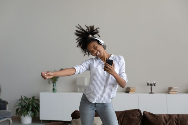 Happy overjoyed teen African girl in headphones listening to music