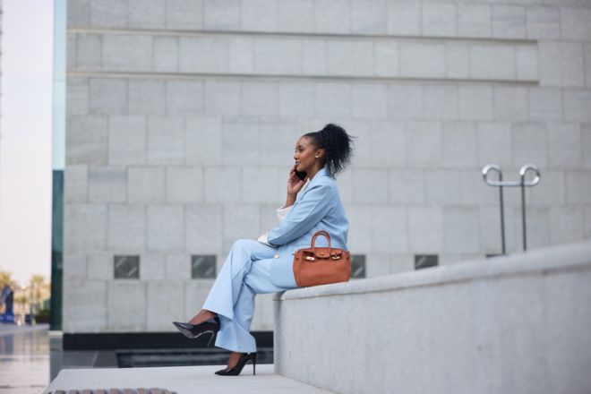 Elegant businesswoman in light blue suit sitting and using her smartphone