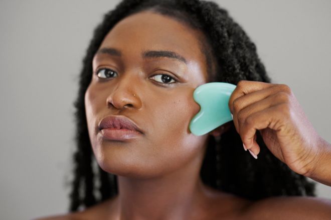 Serious Young Black Woman Using Green Gua Sha Stone for Facial Massage - Horizontal