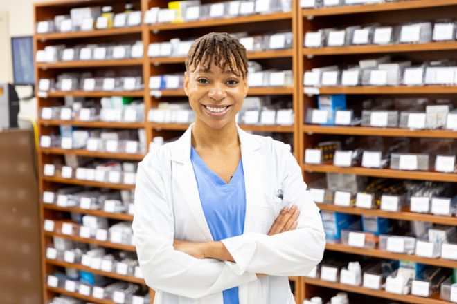 Young black female pharmacist portrait in front of shelves of pills and prescriptions
