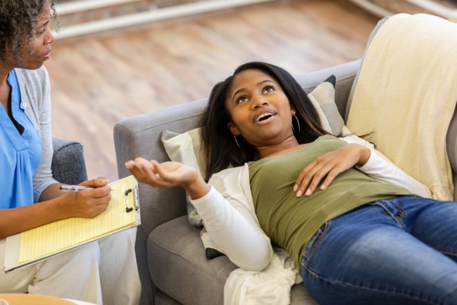 Teenager confides in mental health professional during therapy session while lying on couch.