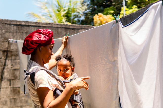 Mother hanging laundry with baby girl in carrier