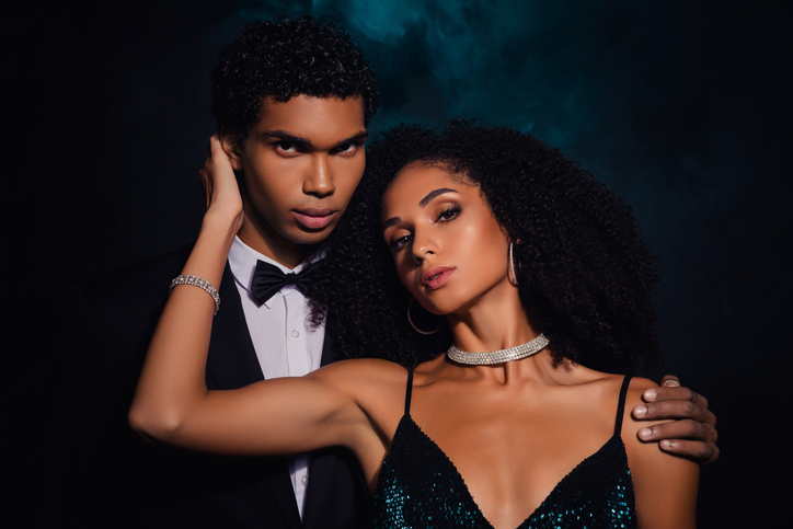 Elegant couple posing in glamorous attire, sense of luxury and sophistication, against a moody green and black backdrop