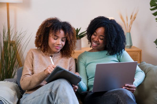 Two women collaborating on laptop and tablet at home