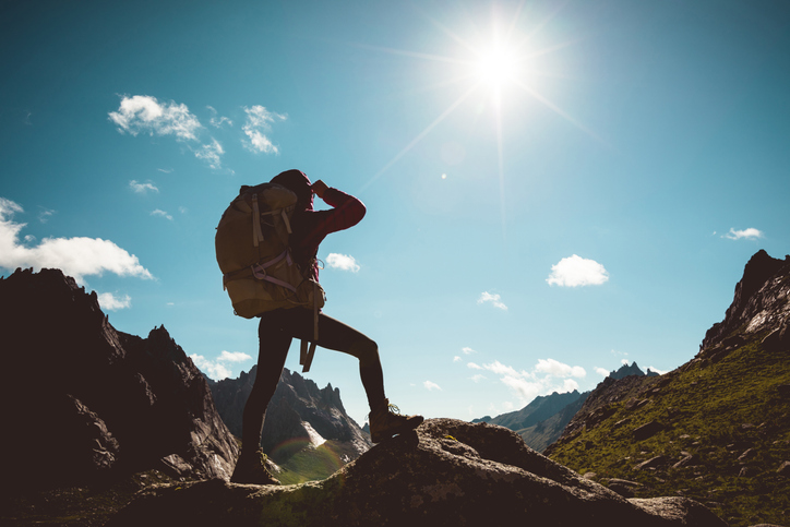 Silhouette of woman with backpack hiking on sunrise mountain top