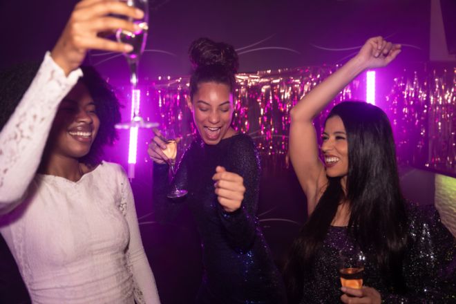Happy friends dancing and celebrating with champagne in nightclub