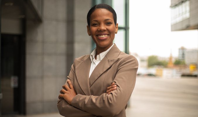 Confident businesswoman smiling with arms crossed in front of office building