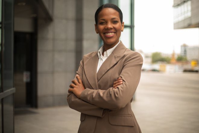 Confident businesswoman smiling with arms crossed in front of office building