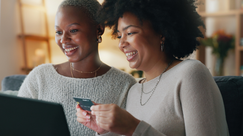 Payment, credit card and friends online shopping on a laptop for discount or sale on a digital fintech website at home. Ecommerce, happy and excited African women on the sofa banking on the internet