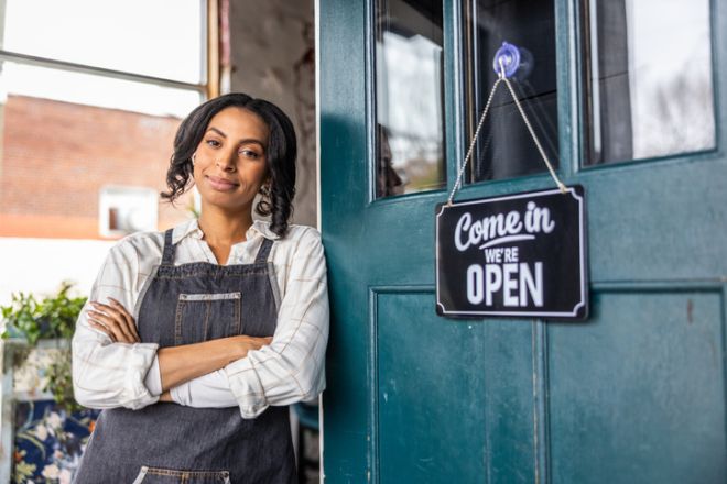 Portrait of young woman hanging an open sign on door of her shop