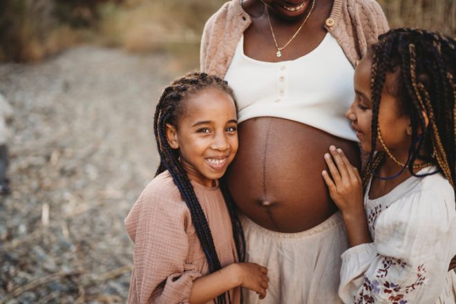 Happy smiling mix race girls hugging black pregnant mom belly
