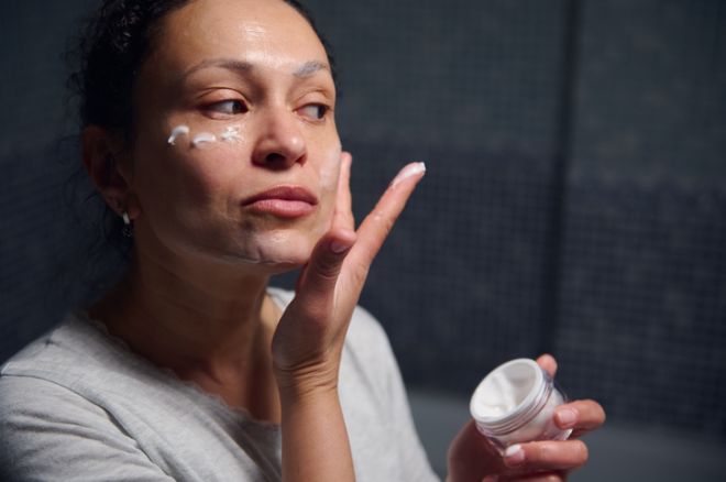 Middle-Aged Woman in Pyjamas Applying Face Cream During Morning Skincare Routine at Home