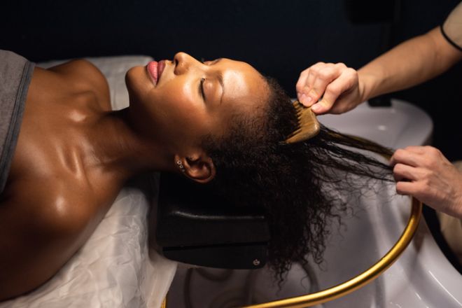 Beautiful African American woman is enjoying hair washing and treatment at salon