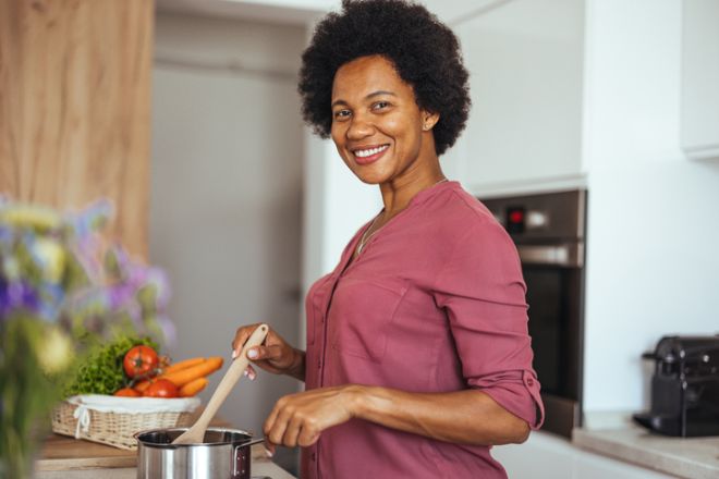 Smiling Woman Cooking a Healthy Meal in Modern Home Kitchen Stirring a Sauce Pot