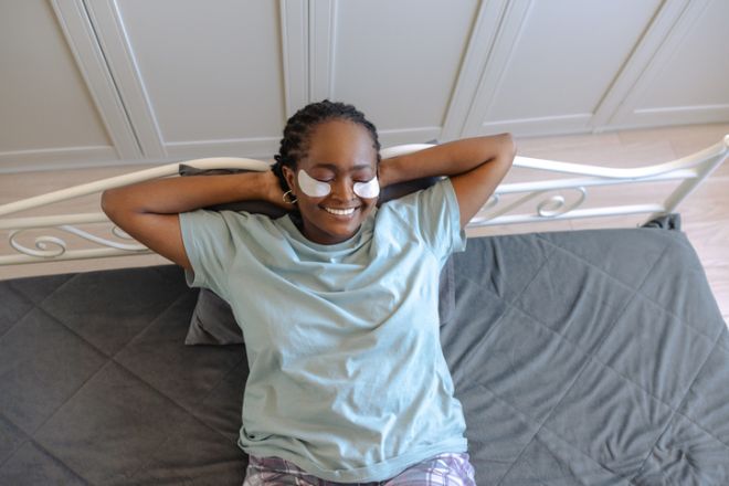 Young woman relaxing on bed with under-eye patches in cozy home setting