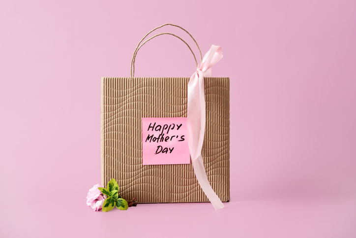 Paper shopping bag with Happy Mothers Day sticker stands on pink surface. Mother s Day special offer, seasonal retail discount, Limited time deal, flash sale announcement.