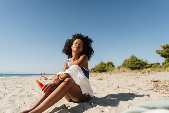 African American woman applying sunscreen spray at the beach
