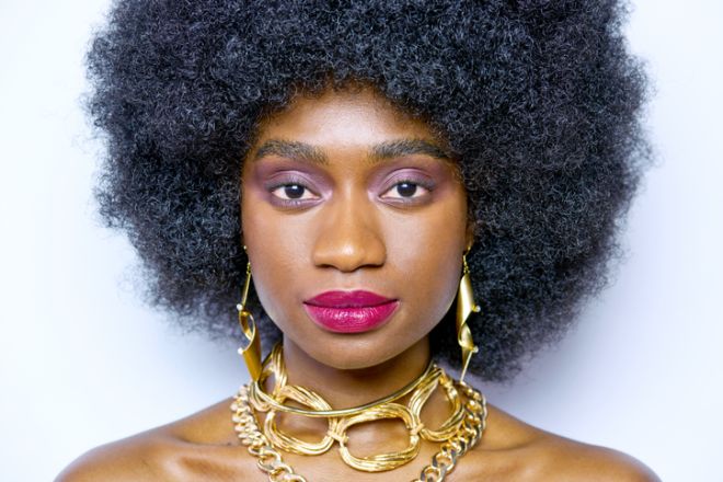 A contemporary studio beauty image with a model wearing an Afro Wig and Gold jewellery.