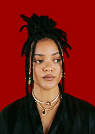 Confident African American Woman with Dreadlocks and Gold Jewelry on Red Background Portrait