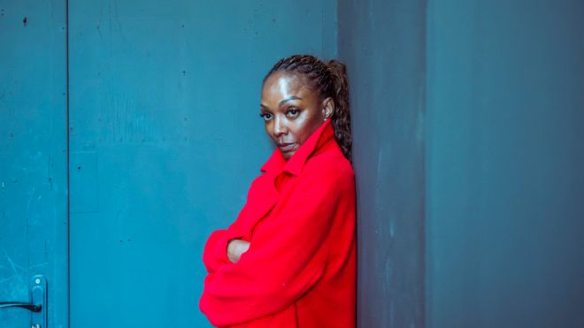 Black woman wearing red coat standing against blue wall