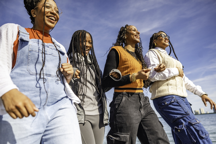 Group of four young African American teens and young adults, sisters or friends, happy outdoor portrait of togetherness, youth and female friendship