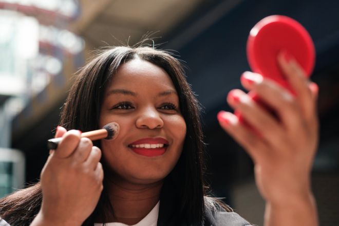 Businesswoman applying makeup with a brush and mirror