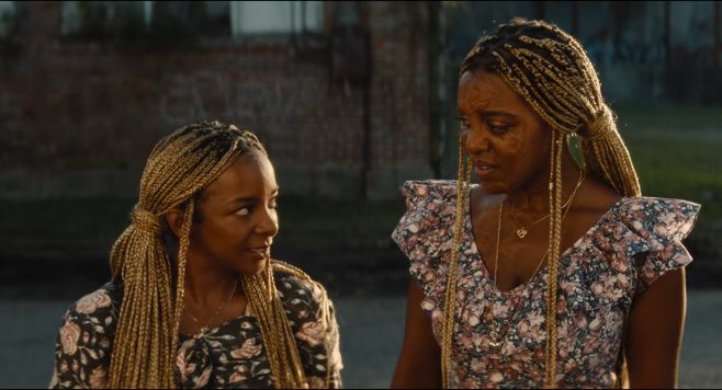 Two women with braided hairstyles standing together outdoors, wearing floral print dresses.
