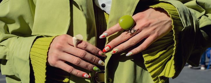 Woman wearing lime green trench coat and sweater, showing trendy patterned nails and fashion rings