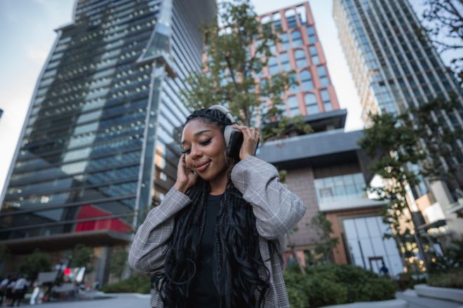 Black businesswoman immersing herself in the music on her wireless headphones amidst tall buildings and bustling city