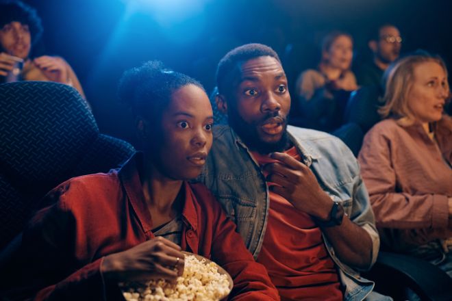 Shocked black couple watching a tense movie at cinema.