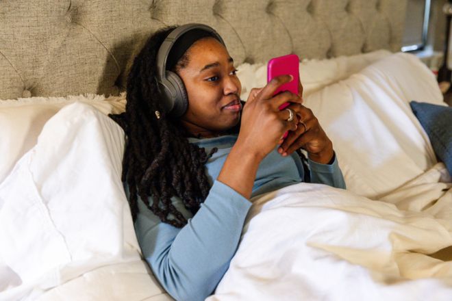 Relaxing Woman in Bed Using Smart Phone and Headphones