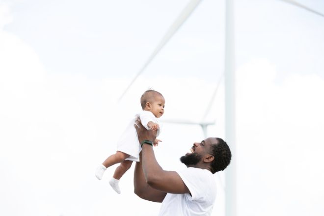 Happy African American family, father, mother and little daughter travel at wind turbine field farm on holiday vacation