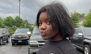 A person wearing a black t-shirt with the Adidas logo standing in a parking lot.