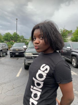 A person wearing a black t-shirt with the Adidas logo standing in a parking lot.