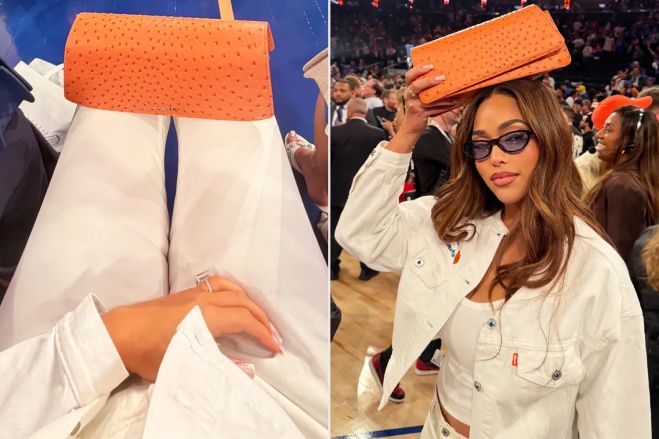 A woman wearing glasses and a white jacket holds a large orange object above her head in a crowded auditorium.