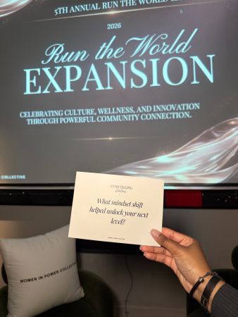 A person holds a card that asks "What mindset shift helped unlock your next level?" in front of a screen displaying the "Run the World Expansion" event logo.
