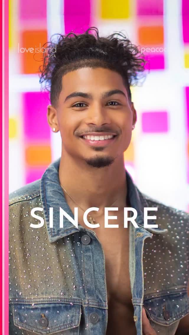 A smiling young man with curly hair wearing a denim jacket with rhinestones, standing in front of a colorful background with the text "love island usa" and "peacock".