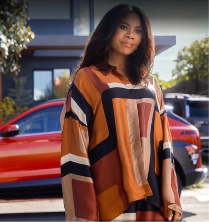 A woman wearing a colorful striped jacket stands in front of a red car.