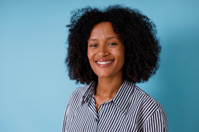 Happy young black woman smiling, posing against a blue background, showcasing natural curly hair and positive emotions