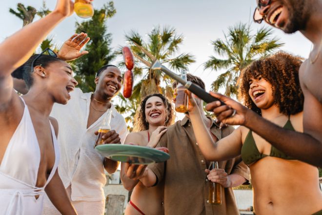 Cheerful friends grilling sausages and enjoying a beach barbecue