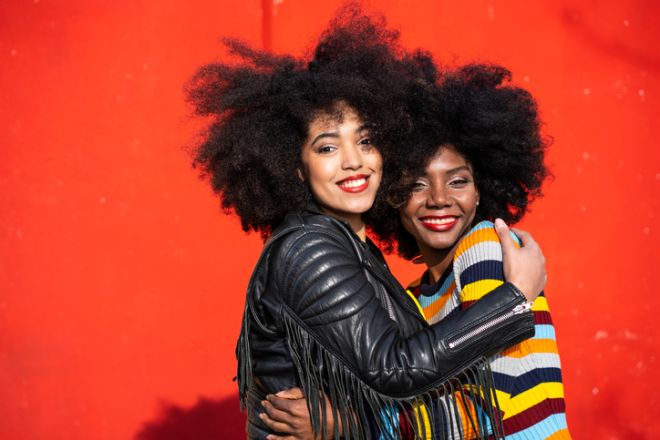 Two black women friends embracing on red background