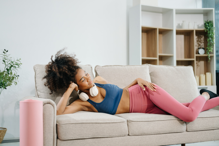 Active woman in athleisure sitting on yoga mat with tablet, headphones and modern home lifestyle.