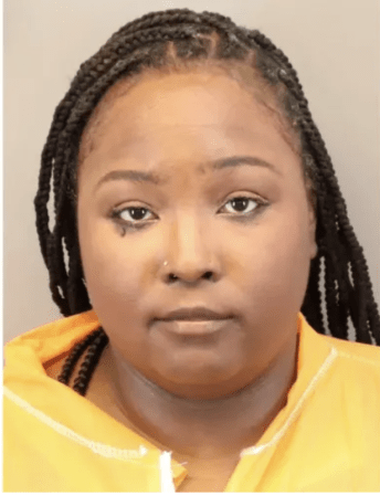 A person with braided hair wearing a yellow jacket looking directly at the camera.