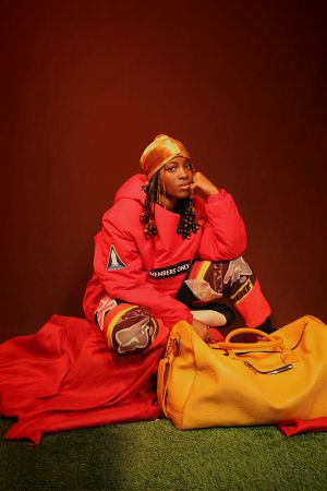A person wearing a red hooded sweatshirt with "MEMBERS ONLY" text, sitting on the floor with a yellow bag.