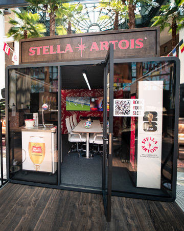 A storefront with a Stella Artois logo and branding, featuring a table and chairs set up inside, along with a QR code and FIFA World Cup signage.