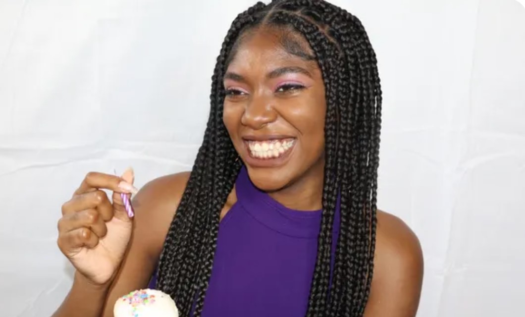 A smiling young woman with braided hair wearing a purple top.